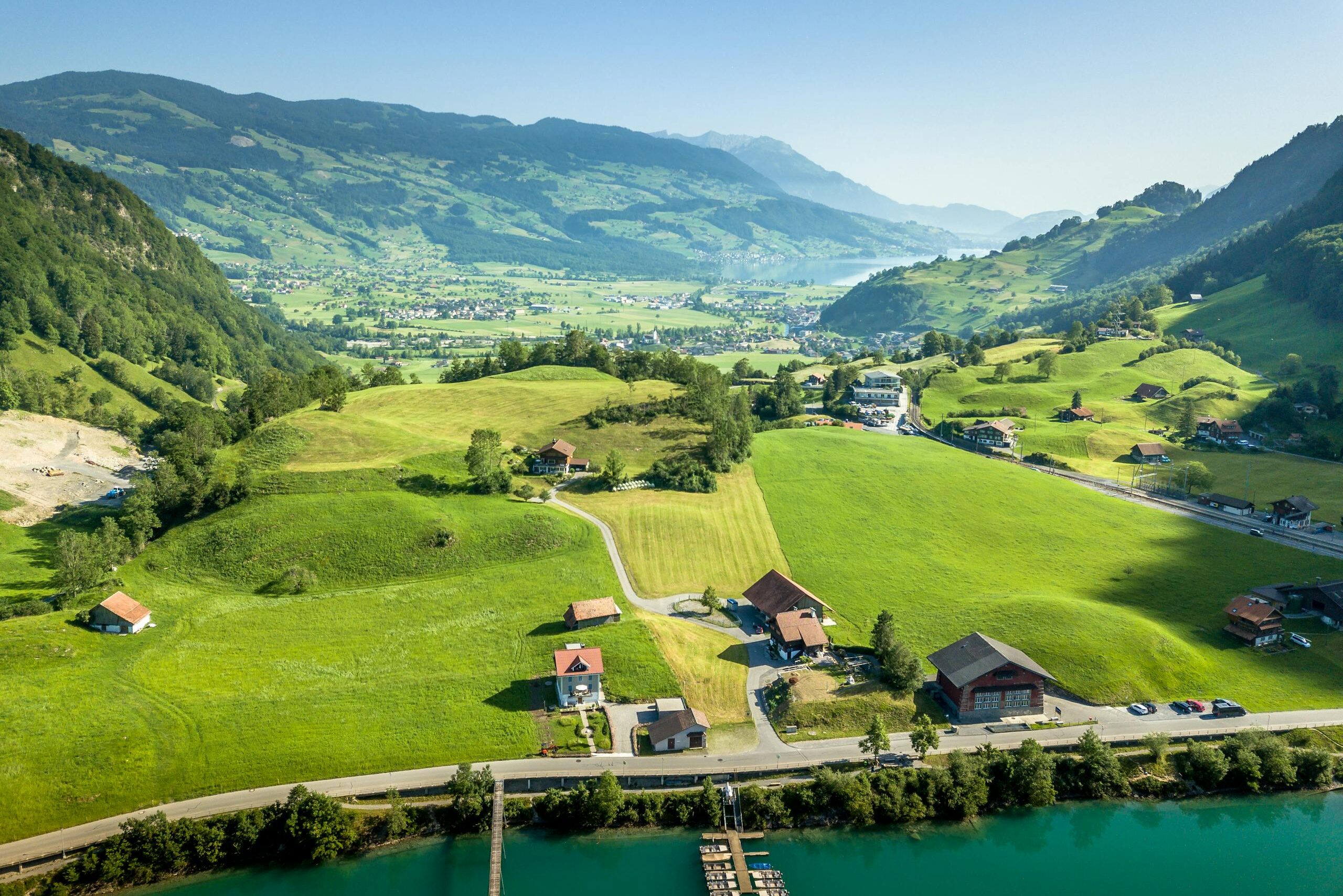 A breathtaking aerial view of the lush Swiss countryside, featuring hills and houses under a clear blue sky.
