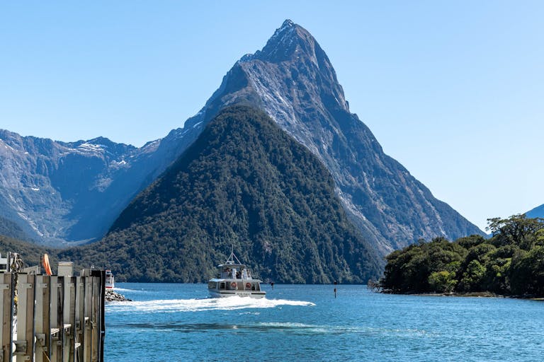 A breathtaking view of Milford Sound with a boat cruising past majestic mountains under a clear blue sky.