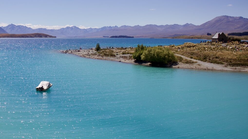 single boat in a bright blue lake with mountains in the distance