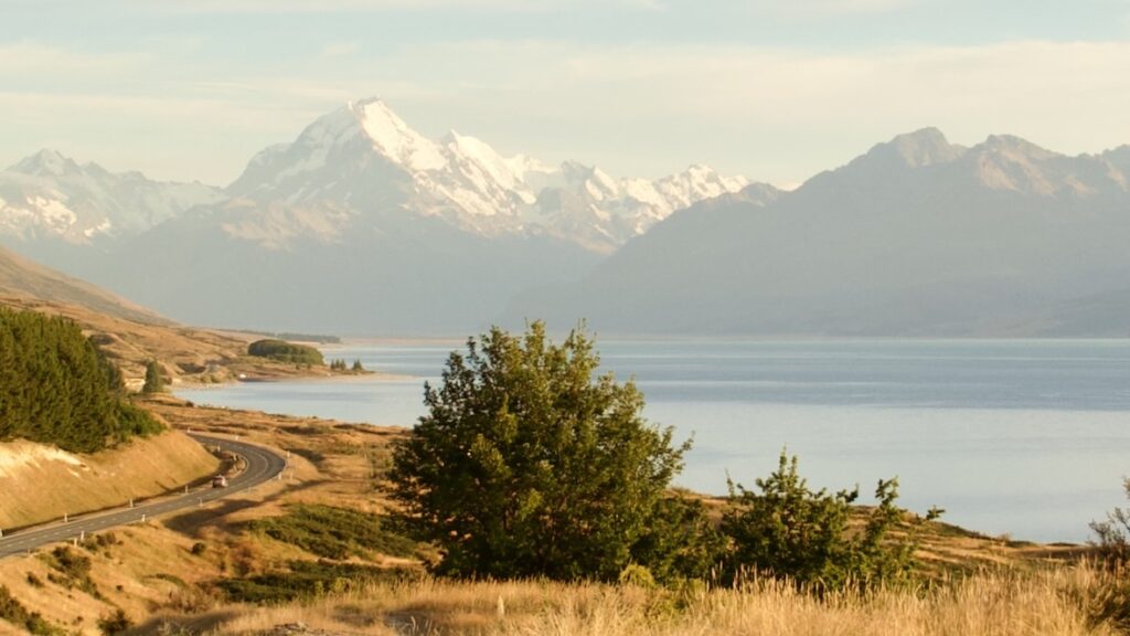mt cook in the distance behind a lake and winding road