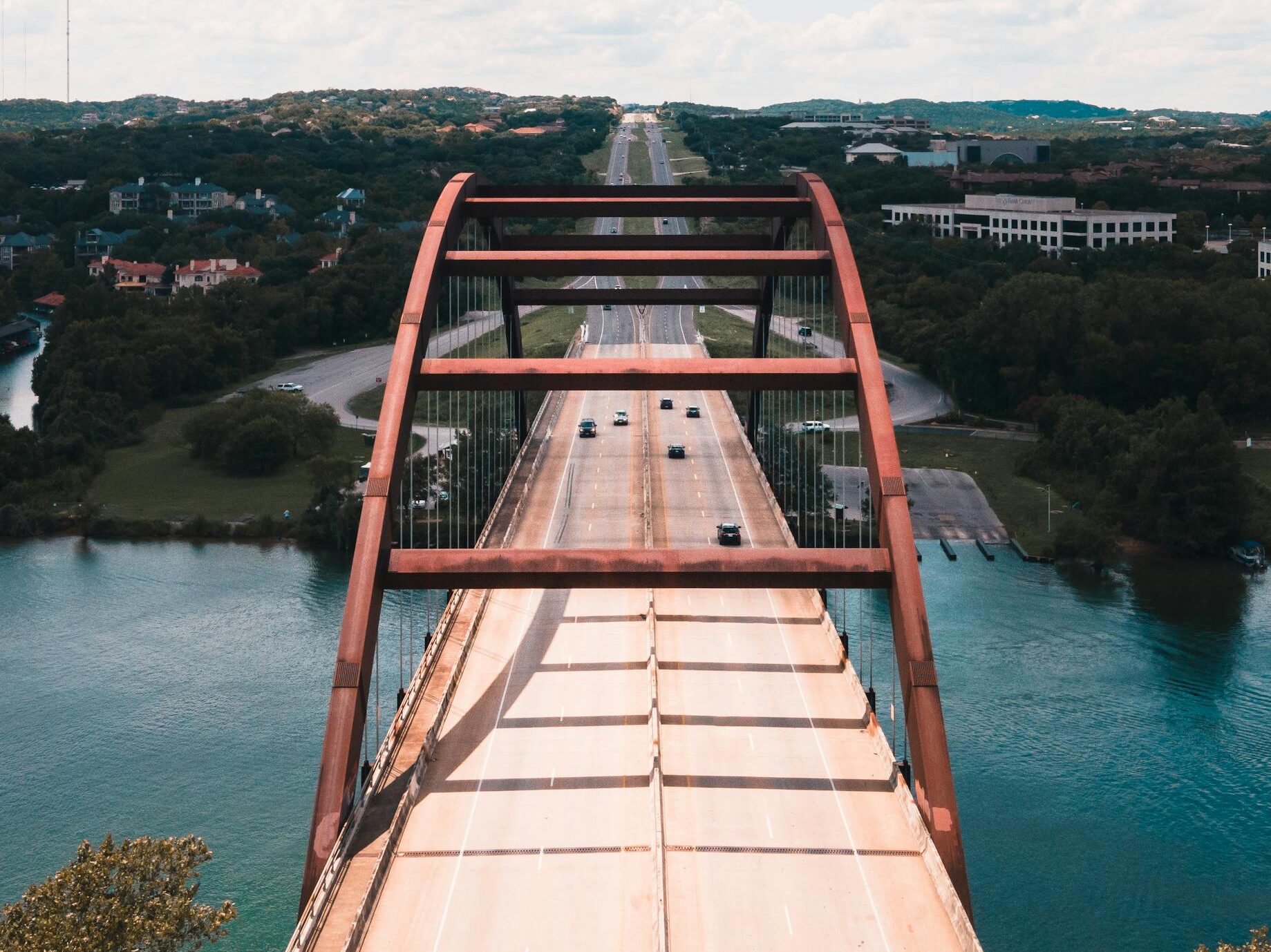 A stunning aerial shot of the iconic Pennybacker Bridge in Austin over the Colorado River on a sunny day.